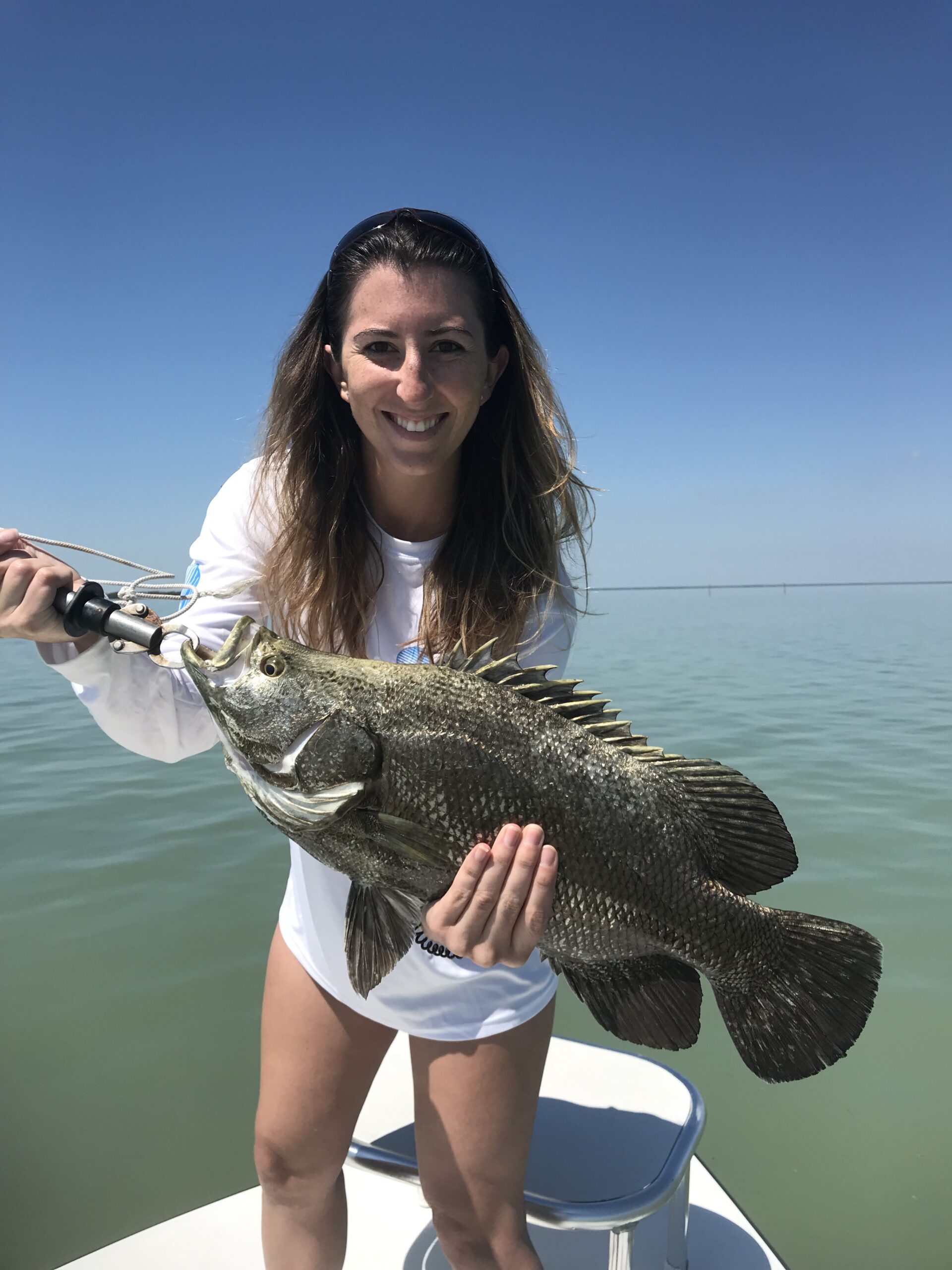 Smiling woman holding a Triple tail fish. Opens a photo gallery.